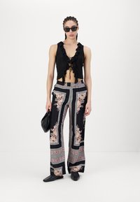 Fekete, fodros nyakú crop top, fekete és virágmintás, bőszárú nadrággal párosítva. A model egy fekete táskát tart a kezében, és napszemüveget visel.