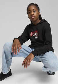 Felpa nera con cappuccio e grafica "Forza Milan", abbinata a jeans baggy azzurri e sneakers nere; texture solide, vestibilità rilassata.