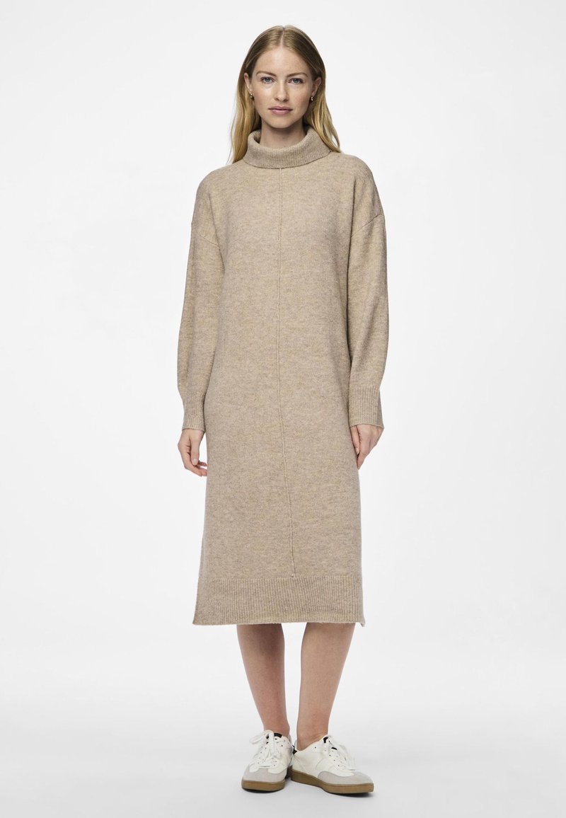 Robe en tricot beige avec un col montant, des manches longues et un ourlet côtelé. Texture douce, conception mi-longue, assortie à des baskets blanches.