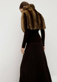 Un chal de piel sintética marrón se deja caer sobre una blusa negra de manga larga y una falda a juego, que presenta una silueta ajustada y un tejido texturizado.