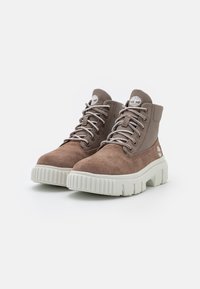 Bruine suède enkelboots met lichtgrijze veters, een gevoerde kraag en een stevige off-white zool, met een logo op de tong en de zijkant.
