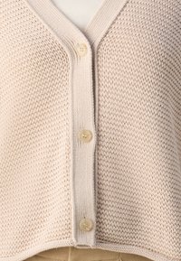 Cardigan beige a maglia con scollatura a V, dotato di chiusura a bottoni, motivo testurizzato e bordo a coste in contrasto lungo i lati.