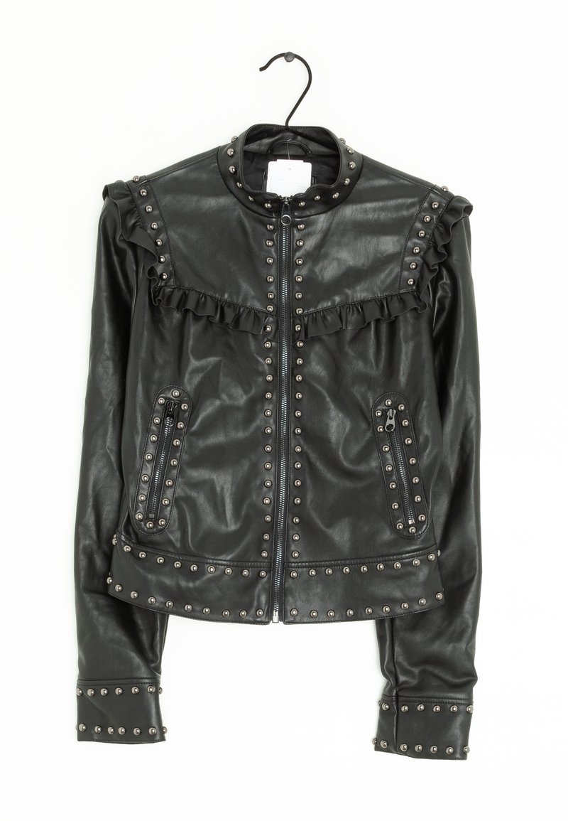 Veste en cuir noire avec fermeture éclair, ornements cloutés, détails à volants sur les épaules et poches zippées, suspendue sur un cintre noir.