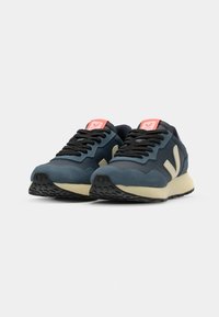 Blue and gray athletic shoes with black laces, a beige midsole, and contrasting orange accents on the tongue and side logo. Rubber outsole.