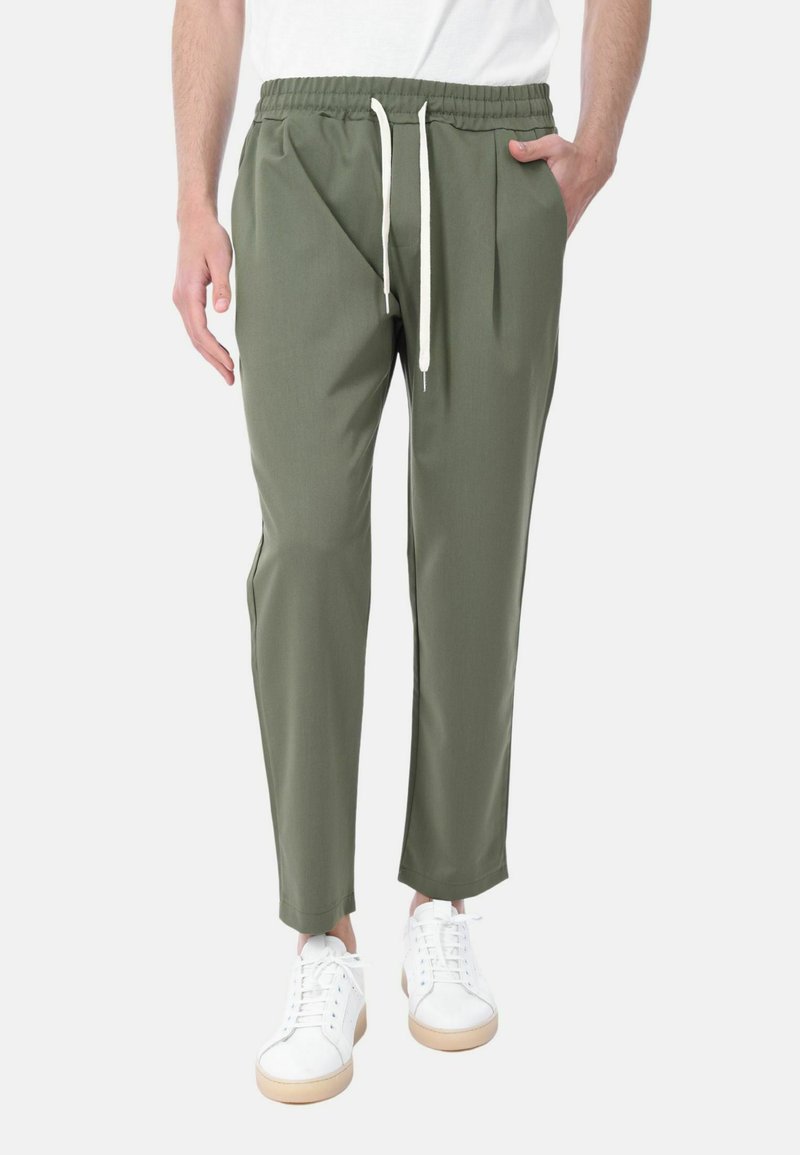 Pantaloni verdi con elastico in vita e cordoncino, vestibilità affusolata, tasche laterali e texture liscia. Abbinati a sneaker bianche.