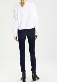 Sudadera blanca recortada de mangas largas combinada con jeans skinny azul oscuro. Botines negros con un tacón grueso completan el look.