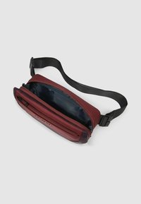 Borsa a tracolla color marrone ramato con tasca frontale con cerniera, tracolla nera e una texture liscia. Interno con fodera blu scuro senza motivi.