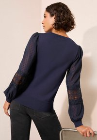 Laevast sinine kampsun õhuke läbipaistvate, palli muster ja pitsdetailidega õlgadel. Soonikkoes ääred ning varrukad. Sobitatud tumedate teksadega.