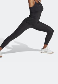 Schwarzes sportliches Tanktop und Leggings aus dehnbarem Material, kombiniert mit weißen Sneakers mit hellbraunen Sohlen.
