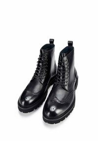 Czarne skórzane botki za kostkę z detalami w stylu brogue, z przodem na sznurówki i uchwytami. Gruba gumowa podeszwa dla lepszej przyczepności i trwałości.