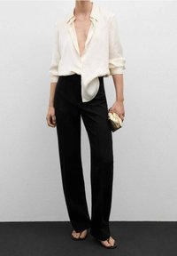 Blouse en soie légère à coupe ample et design à boutons, associée à un pantalon noir taille haute et une pochette métallique dorée.