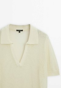 Polo tricoté à manches courtes de couleur crème, avec un tissage ouvert texturé et un col en V profond.