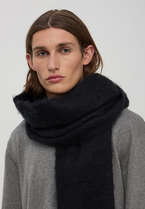 Czarny wełniany szal o miękkim, teksturowanym wykończeniu, owinięty wokół szyi, w połączeniu z szarym swetrem o luźnym, casualowym fasonie.