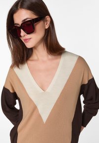 Strickpullover in Beige, Braun und Creme mit einem V-Ausschnitt. Verfügt über geometrische Farbkombinationen und lange Ärmel. Der Stoff wirkt weich.