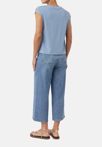 Jasnoniebieska koszulka z krótkim rękawem, luźny fason, w połączeniu z szerokimi jasnoniebieskimi spodniami culottes i beżowymi sandałami na paski.