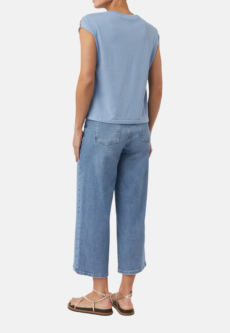 Jasnoniebieska koszulka z krótkim rękawem, luźny fason, w połączeniu z szerokimi jasnoniebieskimi spodniami culottes i beżowymi sandałami na paski.