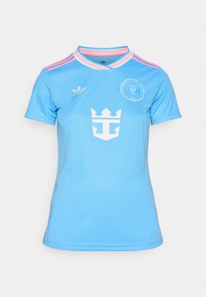 Svetlomodrý futbalový dres s krátkymi rukávmi, s bielymi vertikálnymi pruhmi, korunkovým logom a kruhovým tímovým emblémom na hrudi.