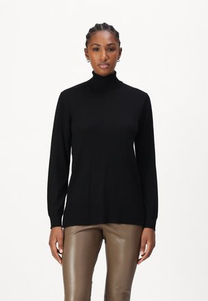 Black turtleneck sweater in a smooth knit fabric with long sleeves, ribbed cuffs, and a relaxed fit, paired with fitted brown pants.