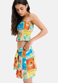 Conjunto de dos piezas con un top cortado y colorido y una falda envolvente a juego, con estampados tropicales en naranja, azul, amarillo y verde.
