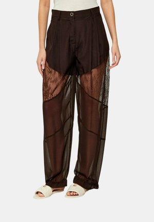 Pantaloni neri a vita alta con pannelli in pizzo trasparente sopra i pantaloncini, portati con sandali bianchi trapuntati.