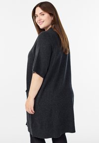 Tamsiai pilka megzta suknelė trumpomis rankovėmis, laisvo kirpimo, su šoninėmis skeltukėmis. Minkštas audinys, apvalus kaklo iškirpimas ir minimalios detalės.