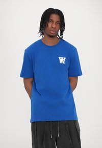 Blue cotton t-shirt with a round neckline, short sleeves, and a white logo "W." on the left chest. Straight cut, soft texture.