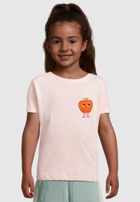 Lys pink bomulds t-shirt med en tegneserieorange med øjne og arme, placeret på venstre side. Korte ærmer og rund halsudskæring.