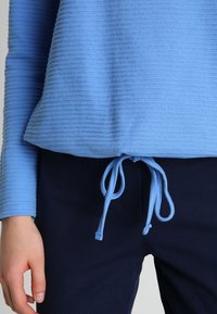 Helles blaues, geripptes Langarmoberteil mit einem Kordelzug in der Taille, kombiniert mit dunkelblauen Hosen. Strukturierter Stoff mit einer lockeren Passform.
