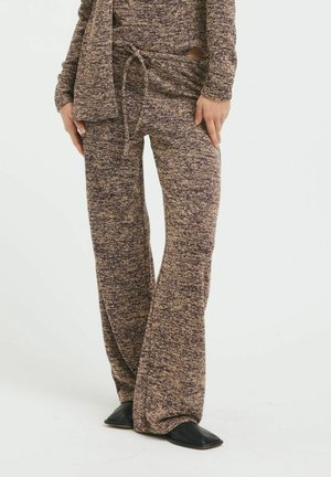 Personne portant un pantalon de détente ample en maille marron et violette chinée avec taille à cordon et chaussures noires à bout carré.