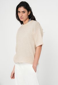 Beige striktrøje med korte ærmer, afslappet pasform og rund halsudskæring, lavet af blødt, struktureret stof med en subtil, naturlig glans.