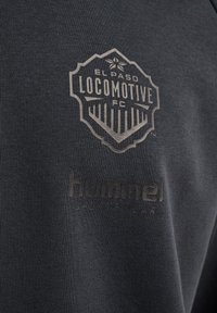 Logo El Paso Locomotive FC oraz nazwa marki Hummel Sportswear nadrukowane na ciemnoszarym materiale.