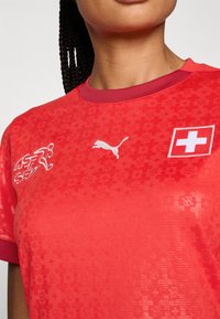 Red sports t-shirt with a textured pattern, featuring white Puma logo and Swiss flag emblem on the chest, and a ribbed crew neck.