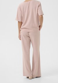 Top leggero di colore rosa chiaro, svasato, con maniche corte e scollatura a barca, abbinato a pantaloni larghi coordinati, realizzati in un tessuto morbido e leggero.
