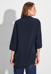 Camicia leggera di colore blu navy, con bottoni, maniche a tre quarti, colletto e orlo curvo. Texture liscia e dettagli minimi.