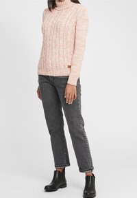 Rosa stickad tröja med hög hals och kabelmönster. Kombinerad med grå jeans och svarta ankelstövlar. Enkelt design och texturerad tyg.