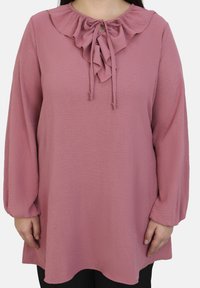 Blusa rosa a maniche lunghe con colletto arricciato e dettaglio a fiocco, caratterizzata da una finitura testurizzata e un fit rilassato che scivola sotto i fianchi.