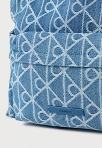 Τζιν σακίδιο πλάτης σε ανοιχτό μπλε με λευκό επαναλαμβανόμενο μοτίβο, ραφές λεπτομέρειας και μπλε ετικέτα με το λογότυπο Calvin Klein.