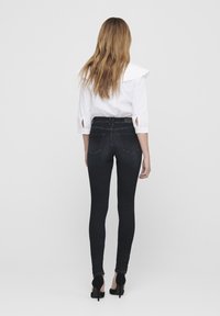 Jeans negros ajustados de cintura alta, combinados con una blusa blanca con cuello ondulado y mangas enrolladas. La textura es suave y entallada.