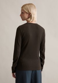 Ciemnobrązowa, prążkowana bluzka z długim rękawem i okrągłym dekoltem. Gładka faktura i dopasowany krój, pokazana od tyłu z subtelnymi detalami szwów.