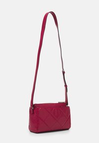 Malá červená prošívaná kabelka přes rameno s nastavitelným popruhem a jemným raženým vzorem, zobrazena na jednobarevném bílém pozadí.