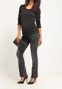 Maglietta nera a maniche lunghe in tessuto elastico. Jeans slim-fit grigio scuro con una texture sbiadita. Clutch nera e décolleté a punta, per un look elegante.
