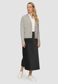 Grauer Cardigan mit Knopfleiste, getragen über einem weißen Hemd und einem schwarzen Midirock. Kombiniert mit weißen Turnschuhen. Einfaches und lässiges Design.
