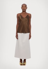 Brun sateng camisole topp med tynne stropper, paret med en lang, ensfarget hvit skjørt og sandaler med gull sløyfe-accenter, båret av en stående modell.