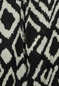 Svart och krämfärgad tyg med ett geometriskt mönster som har djärva former och en texturerad yta, vilket skapar en slående visuell kontrast.