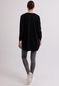 Svart oversized tröja med långa ärmar, tillverkad av mjukt tyg, kombinerad med grå smala jeans och vita sneakers. Bakifrån visas.