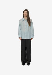 Light blue oversized button-up shirt with vertical stripes, single chest pocket, paired with black wide-leg pants and black shoes.