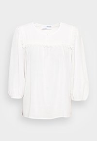 Blusa bianca con scollatura rotonda, maniche a sbuffo e un pannello in pizzo decorativo sul petto. Presenta un dettaglio con bottone al centro.