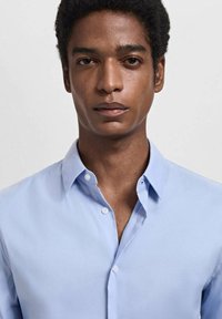 Lichtblauw button-up shirt met een klassieke kraag, een gladde textuur en een subtiele glans. Twee knopen zijn zichtbaar op de kraag.