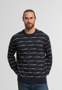 Maglione lavorato a maglia blu navy con strisce orizzontali beige, scollo rotondo e polsini e orlo a coste. Texture liscia con vestibilità comoda.