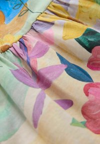Tissu floral avec des motifs vibrants de rose, jaune et vert, présentant une texture douce et un design froncé le long de la couture.